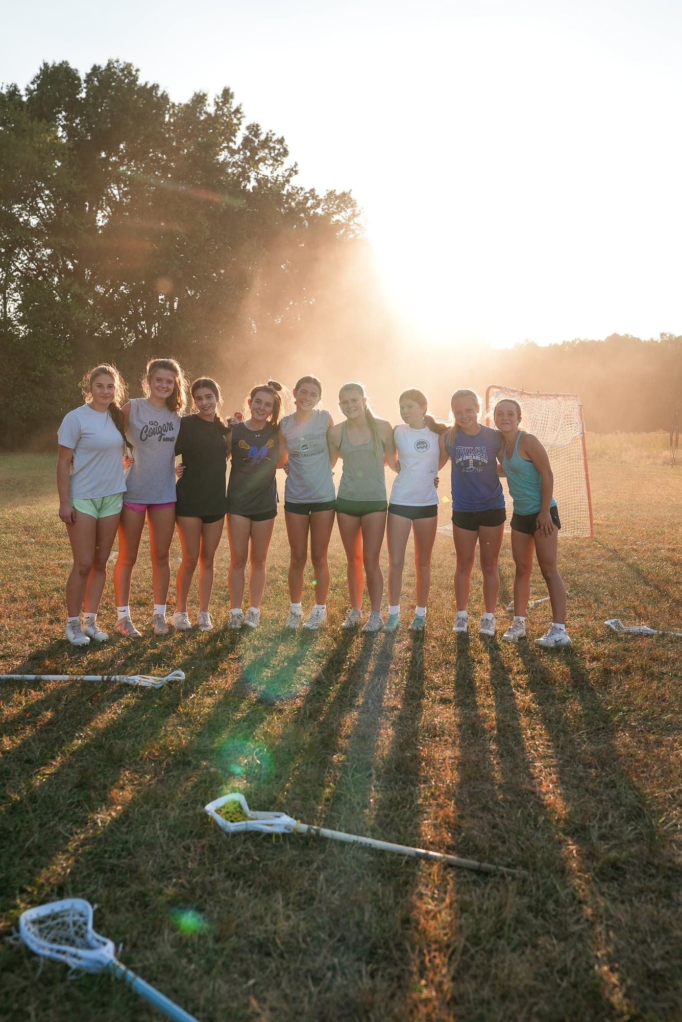 Players standing arm-in-arm at golden hour with a lacrosse goal behind them