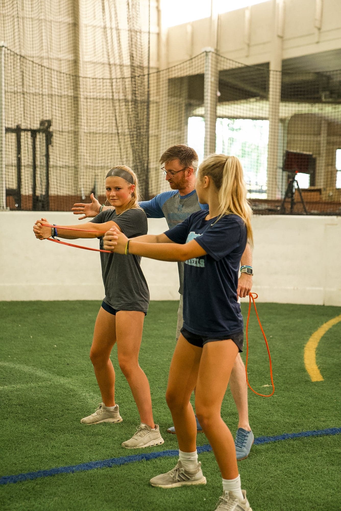 Coach guiding two athletes through resistance band training inside The Barn